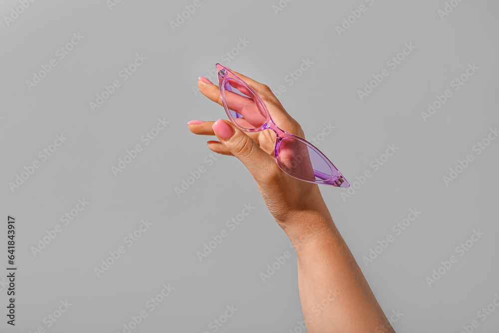 Woman holding stylish sunglasses on grey background