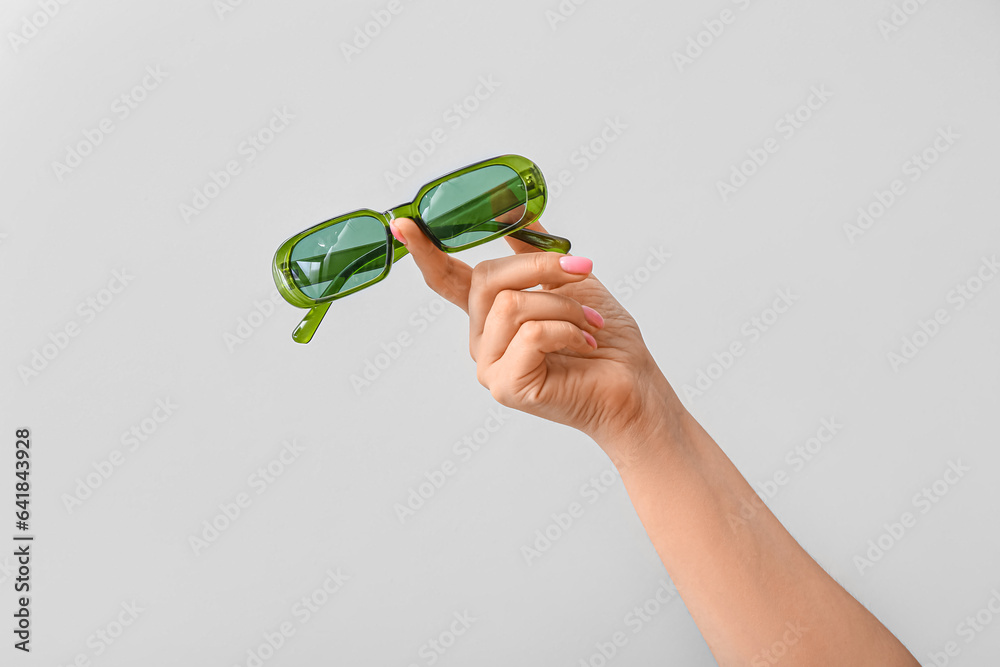 Woman holding stylish sunglasses on grey background