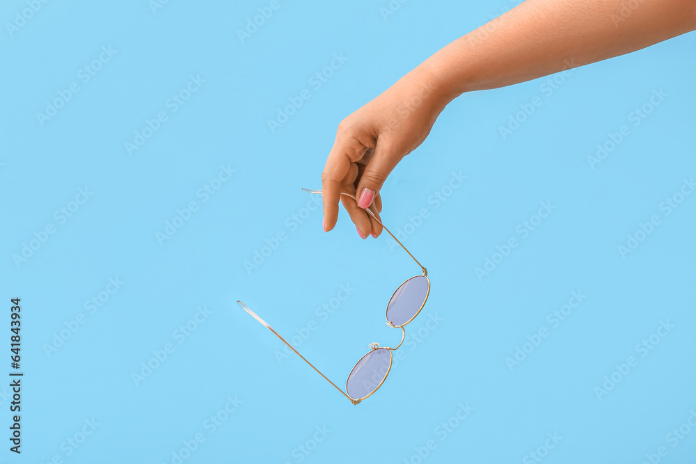 Woman holding stylish sunglasses on blue background