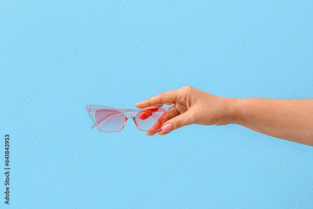 Woman holding stylish sunglasses on blue background