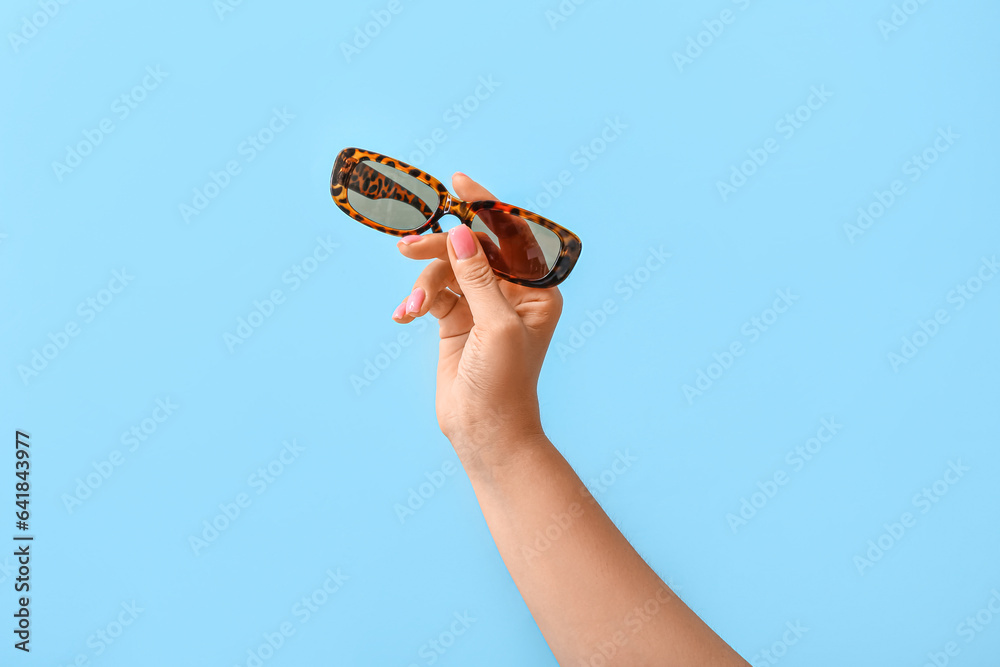 Woman holding stylish sunglasses on blue background