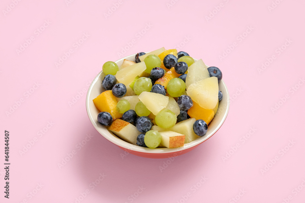 Bowl with fresh fruit salad on pink background