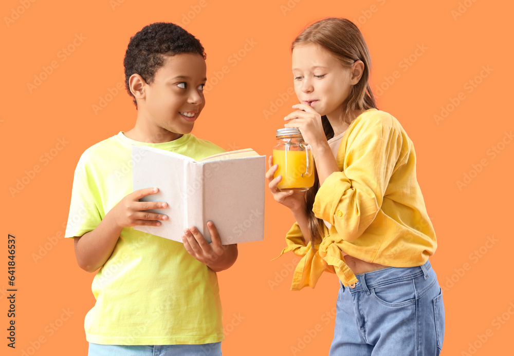 Little children with mason jar of fresh citrus juice reading book on orange background