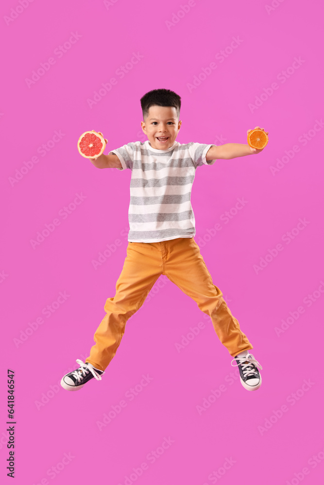 Little Asian boy with slices of fresh grapefruit and orange jumping on purple background