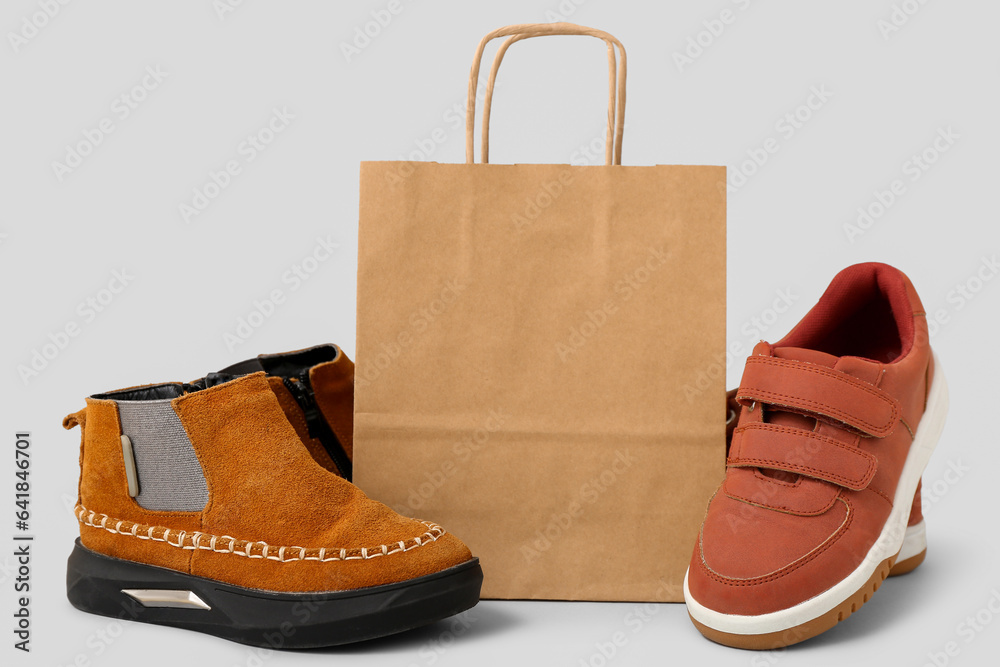 Paper shopping bag with stylish childs shoes on grey background