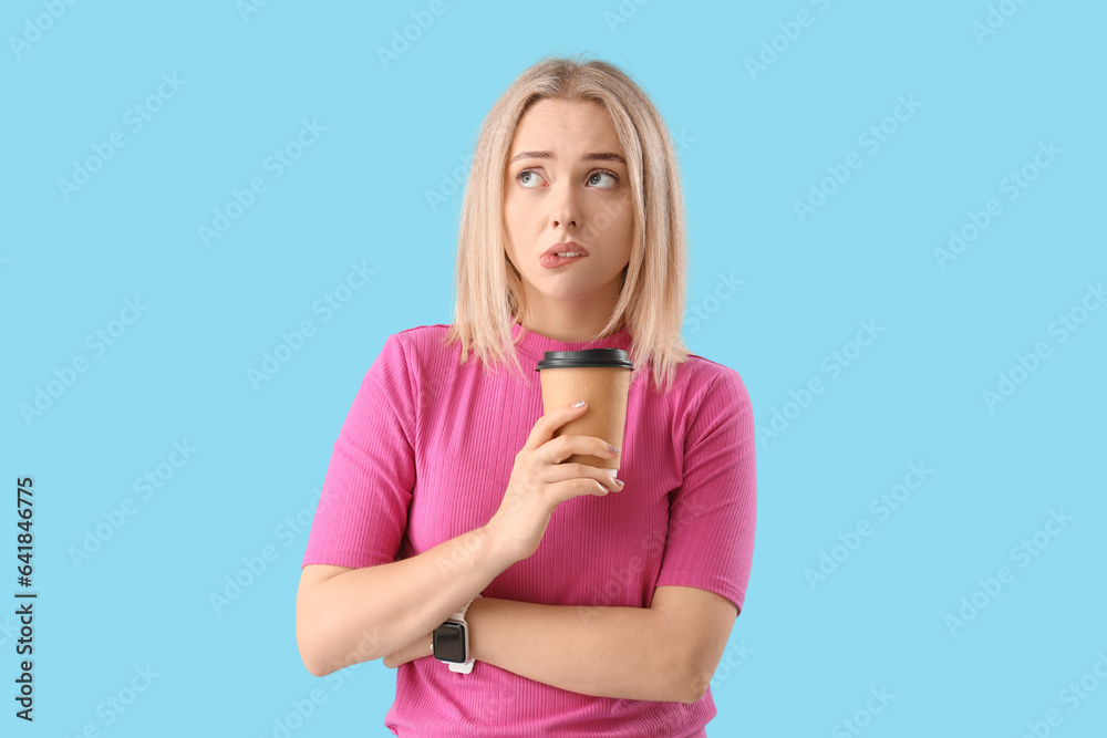 Thoughtful young beautiful woman with cup of coffee on blue background