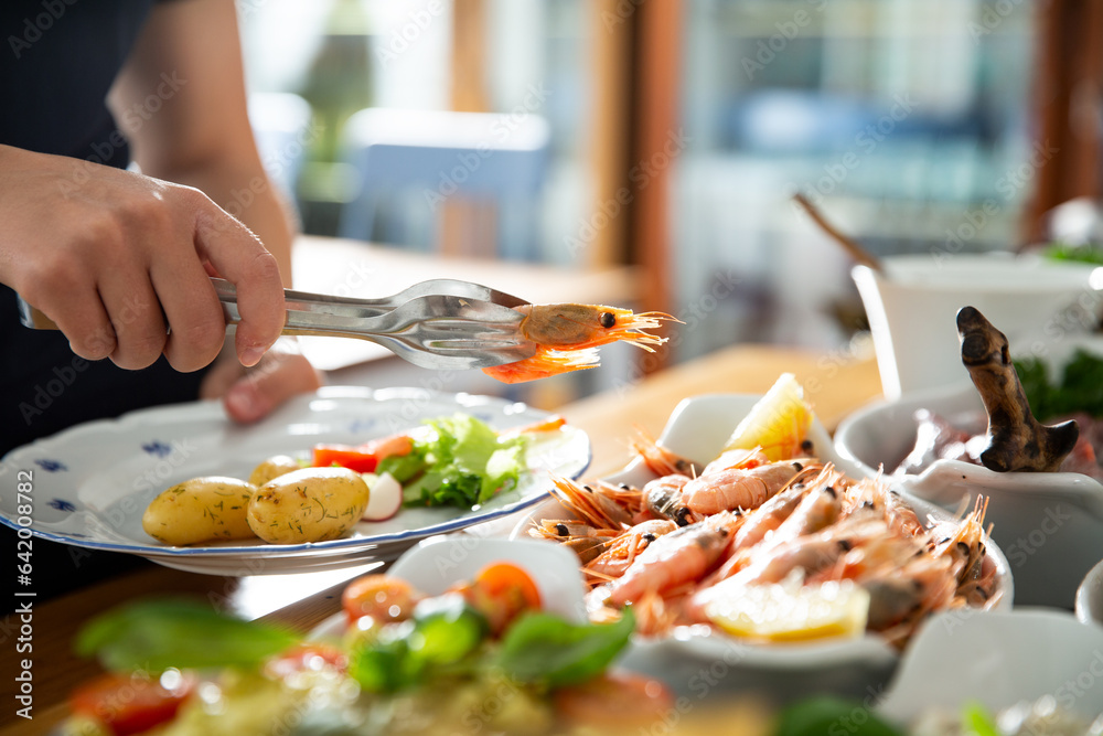 A restaurant customer puts delicious shrimp on a plate. Seafood buffet lunch in a cafe