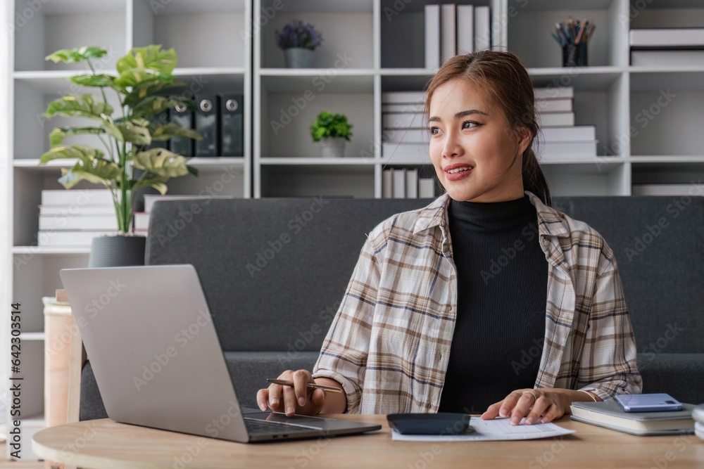 Beautiful and inspired Asian woman working on her tasks on laptop in a living room on the weekend.