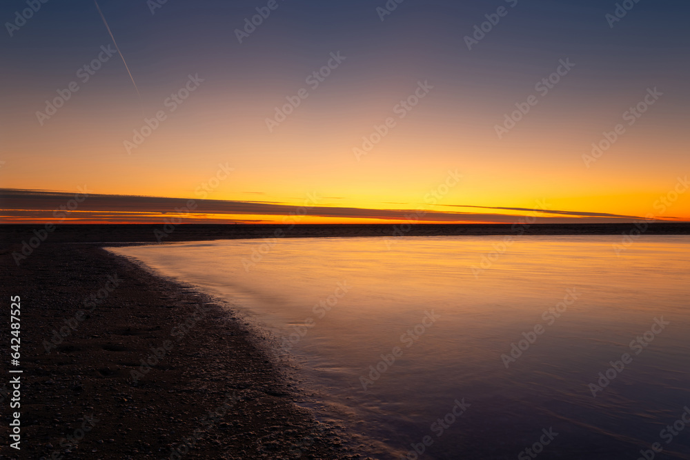 A seascape during sunset. Sand on the seashore. Bright sky during sunset. A sandy beach at low tide.