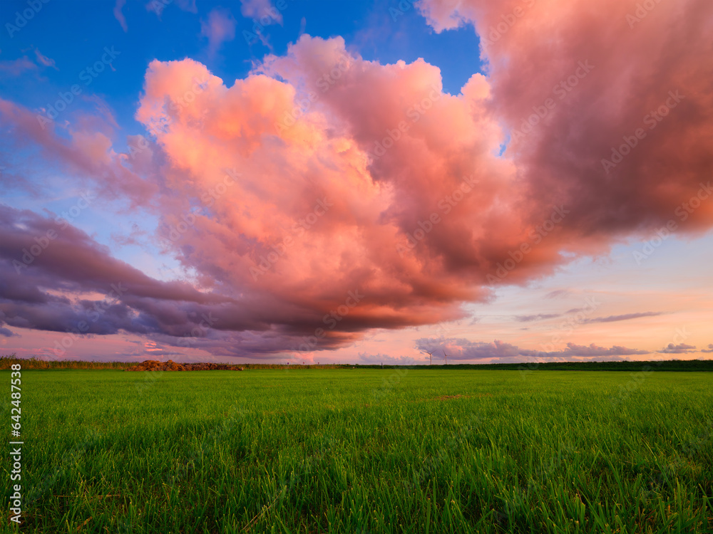 Natural landscape during sunset. Huge pink cloud and blue sky. Field and meadow. Huge cloud in the s