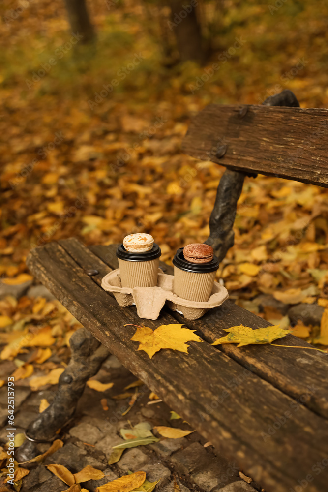 Cups of coffee with macaroons on bench in autumn park