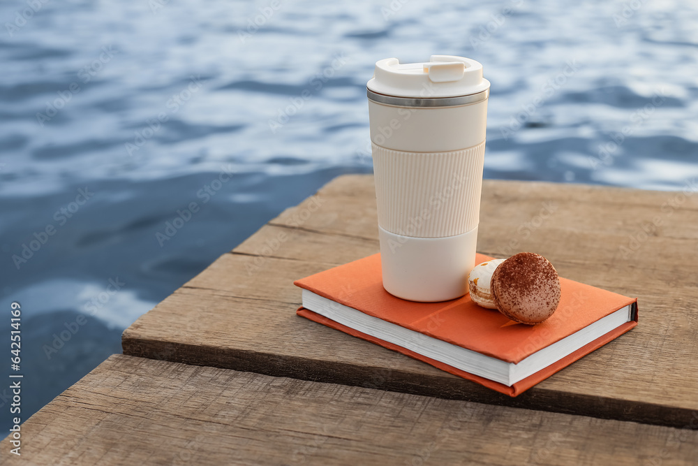 Book with cup of coffee and macaroons on bridge near river