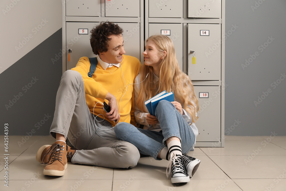 Cute teenage couple with earphones listening to music near locker at school