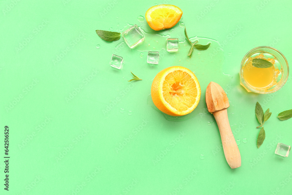 Orange with juicer, glass, ice cubes and mint on green background