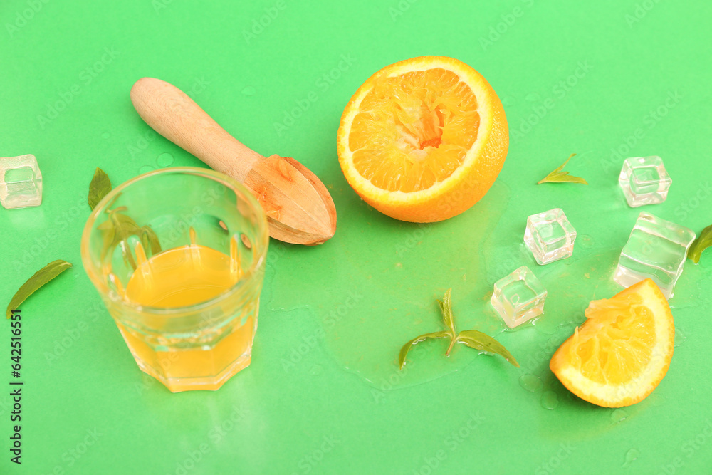 Orange with juicer, glass, ice cubes and mint on green background