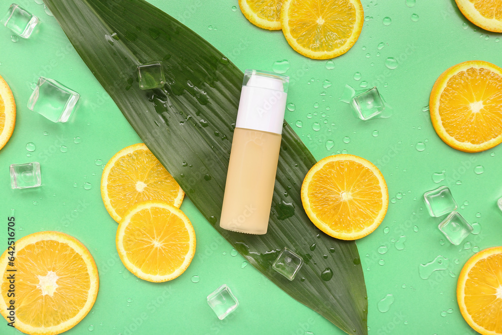 Makeup foundation with orange slices, palm leaf, ice cubes and water drops on green background