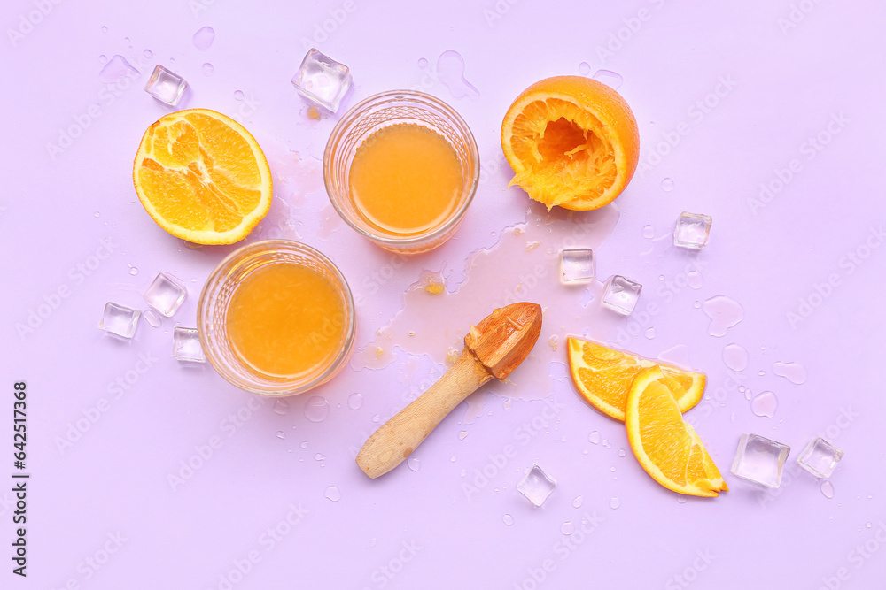 Glasses of orange juice with ice cubes and juicer on lilac background