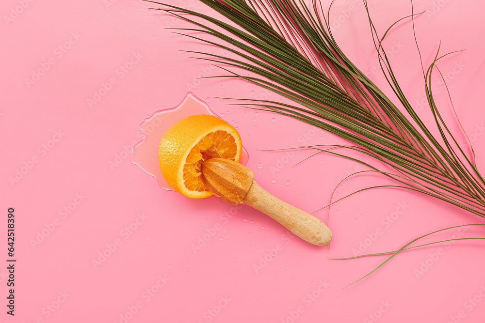 Orange with juicer and palm leaf on pink background