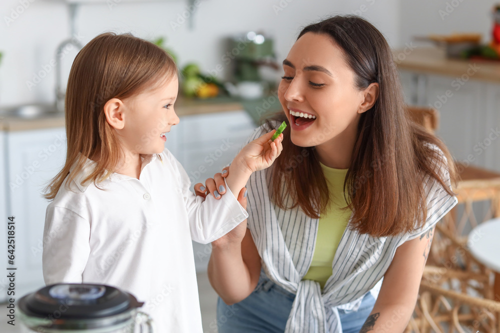 Little girl with her mother eating cucumber in kitchen