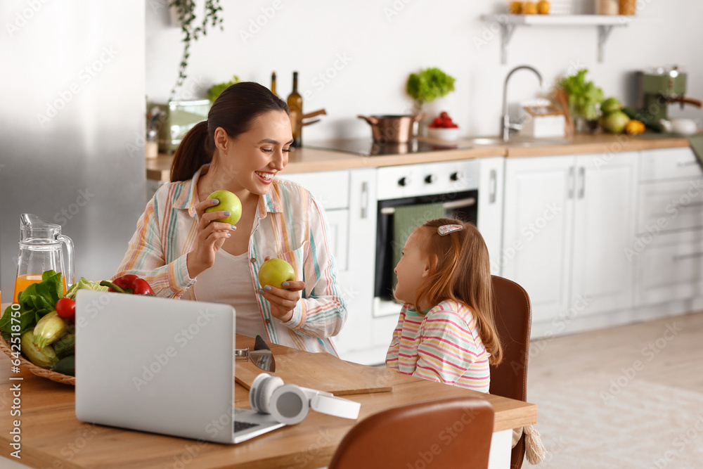 Little girl with her mother and apples in kitchen