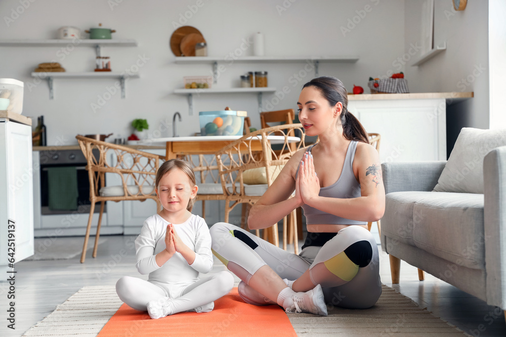 Sporty young woman with her little daughter meditating at home