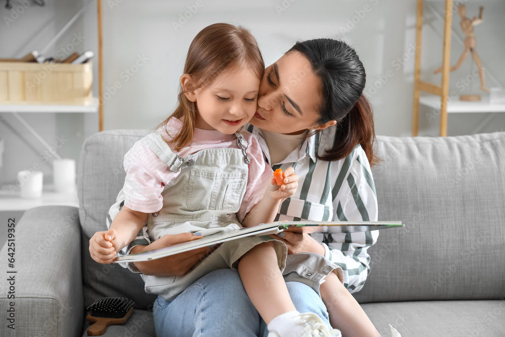 Young woman reading story to her little daughter at home