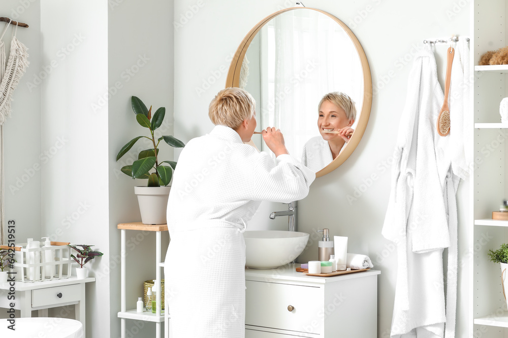 Mature woman brushing teeth near mirror in bathroom