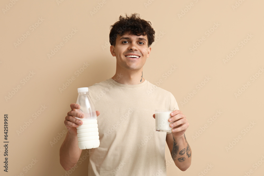 Young man with glass and bottle of milk on beige background