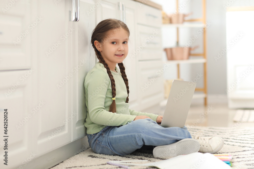 Little girl with laptop studying computer sciences online in kitchen