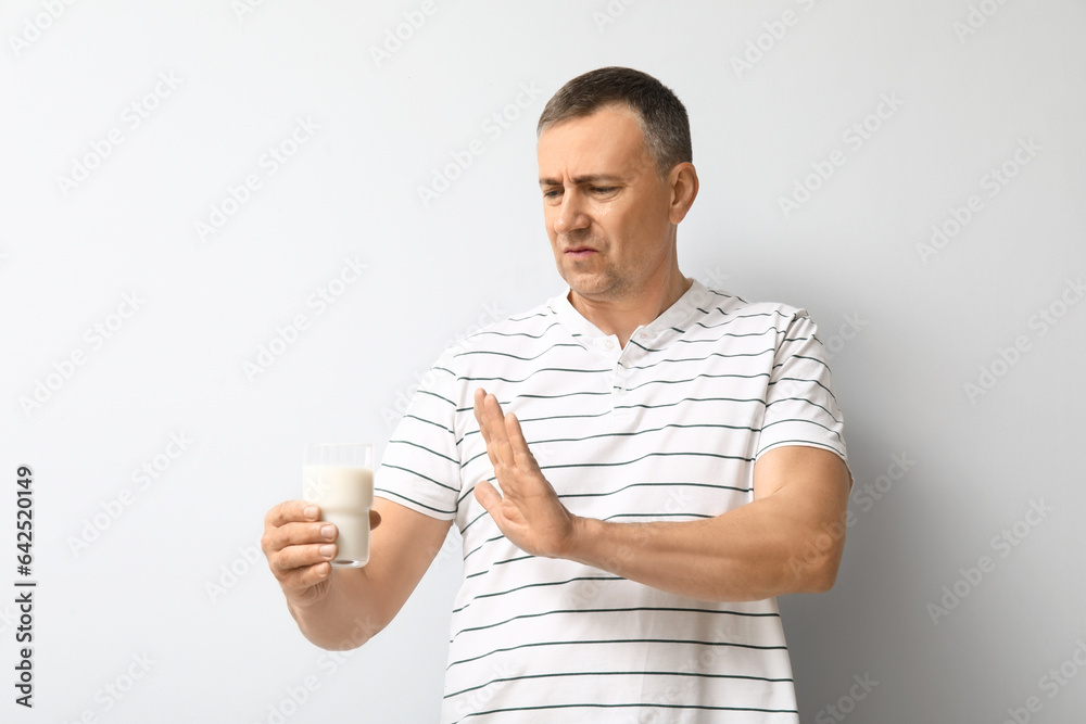 Displeased mature man rejecting glass of milk on white background