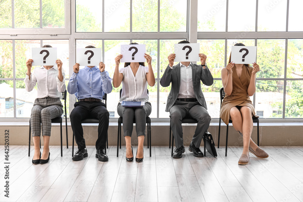 Young people holding paper sheets with question marks while waiting for job interview in office