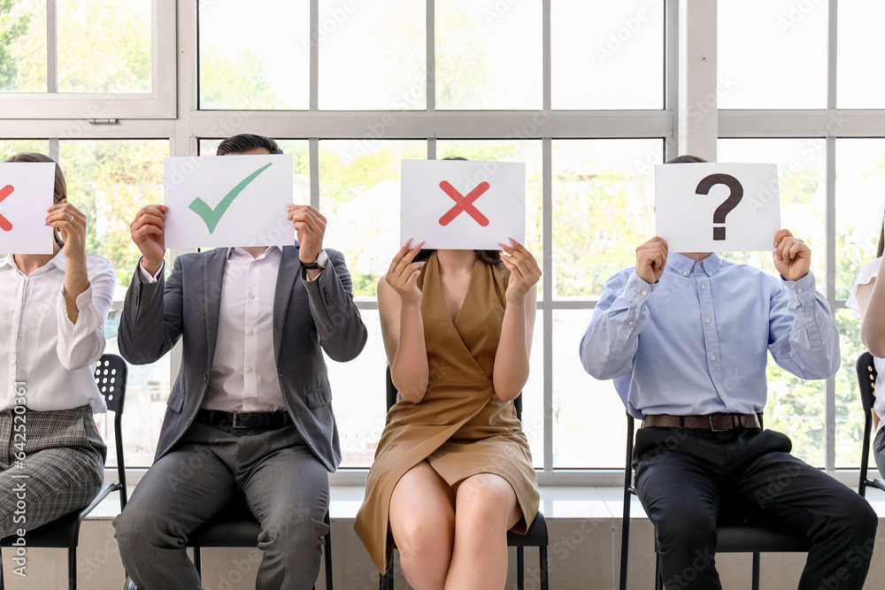 Young people holding paper sheets with different marks while waiting for job interview in office