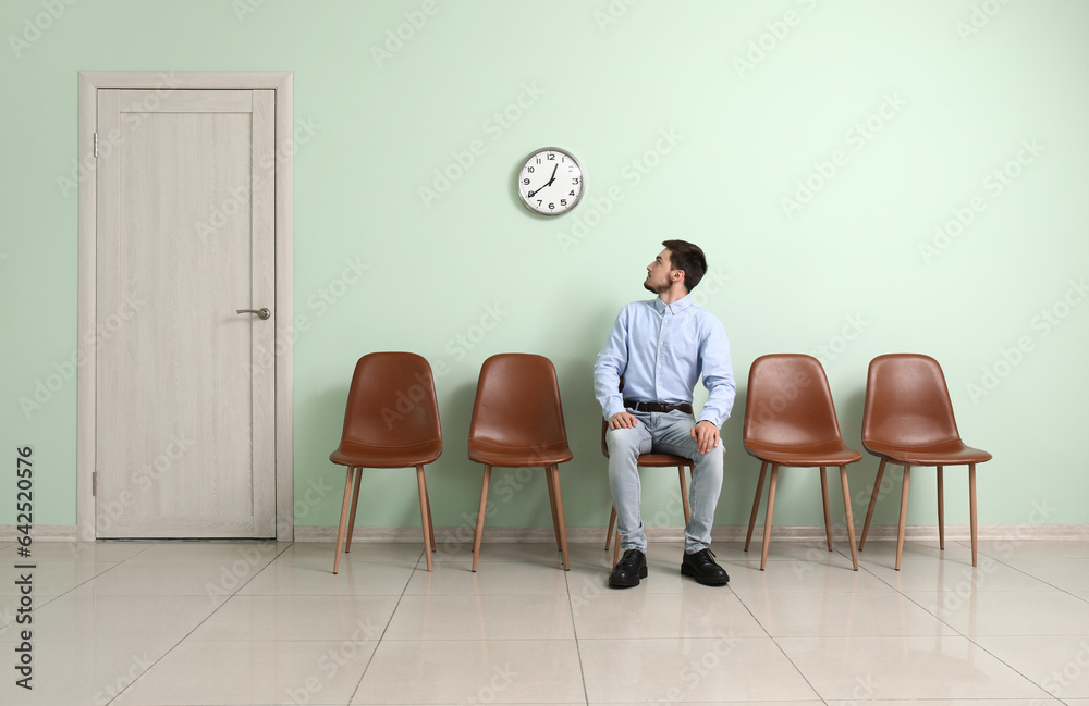 Young man looking at clock while waiting for job interview in room