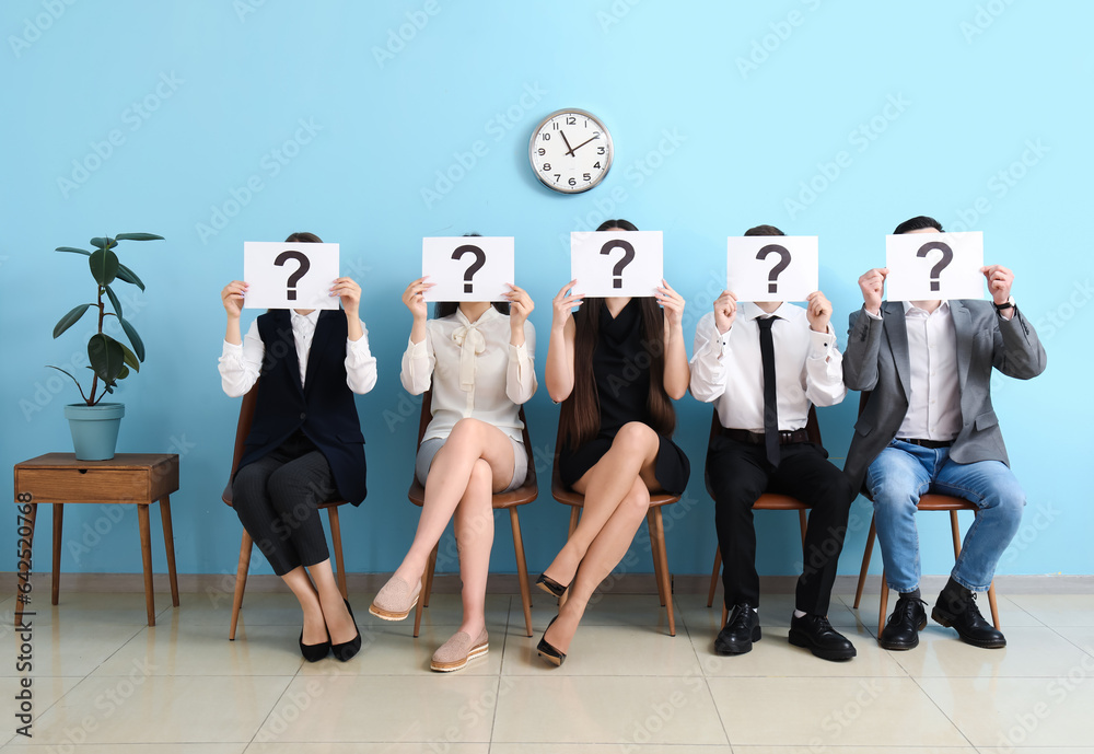 Young applicants holding paper sheets with question marks in room