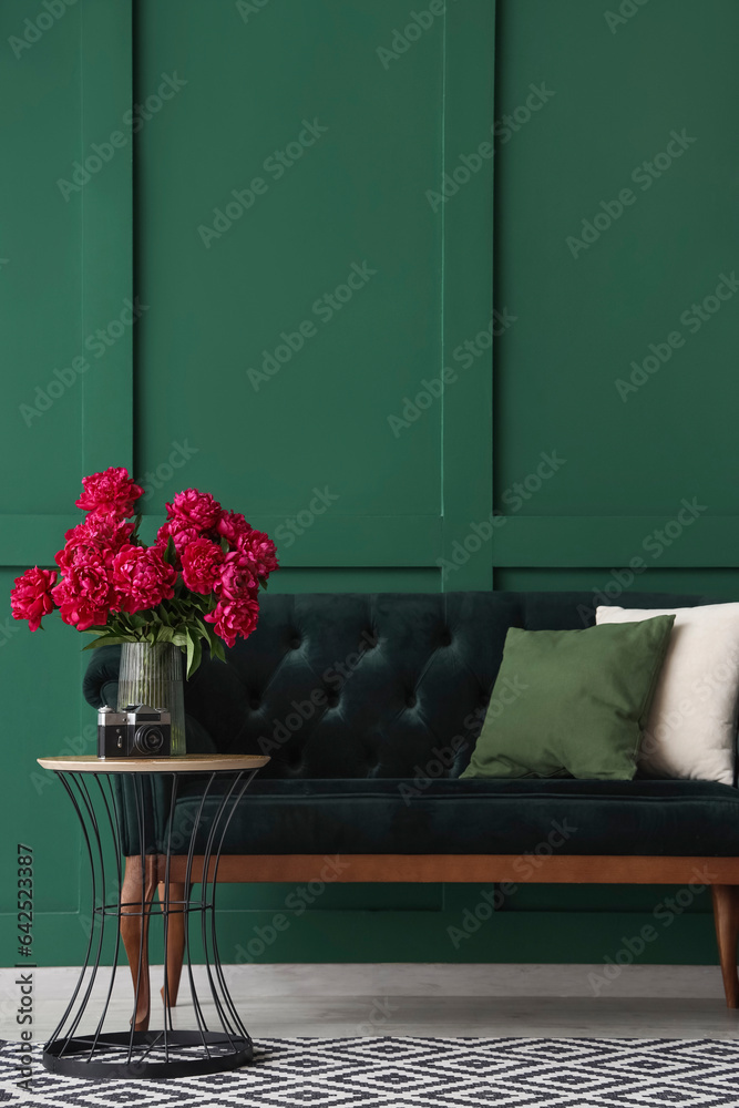 Vase of red peonies with camera, coffee table and couch near green wall