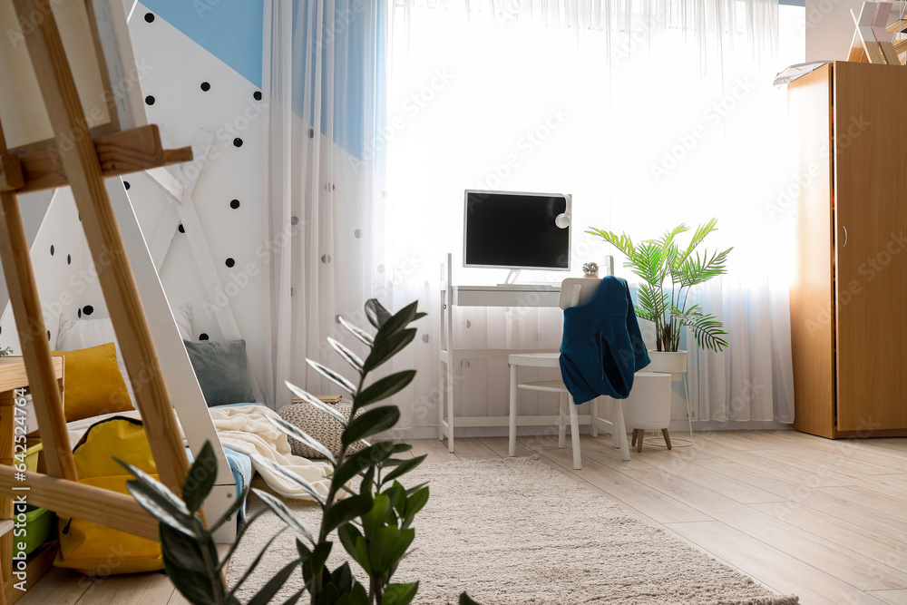 Interior of childrens bedroom with cozy bed, easel and modern computer on desk