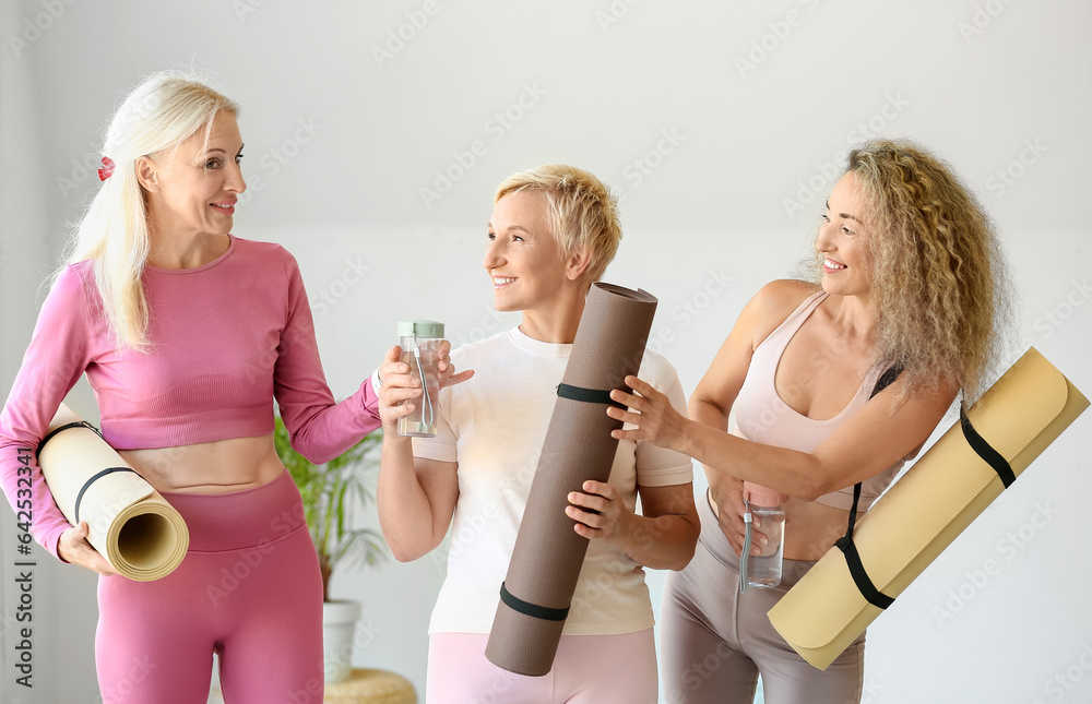 Sporty mature women with yoga mats and bottles of water in gym