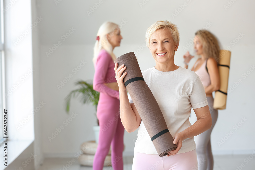 Sporty mature woman with yoga mat in gym