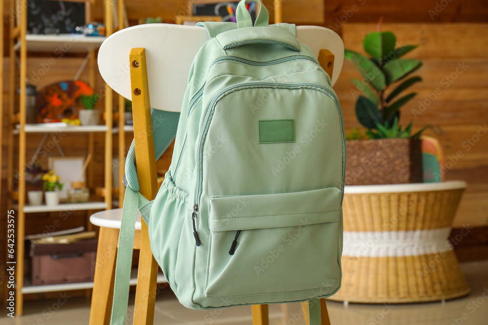 Stylish school backpack hanging on chair in room