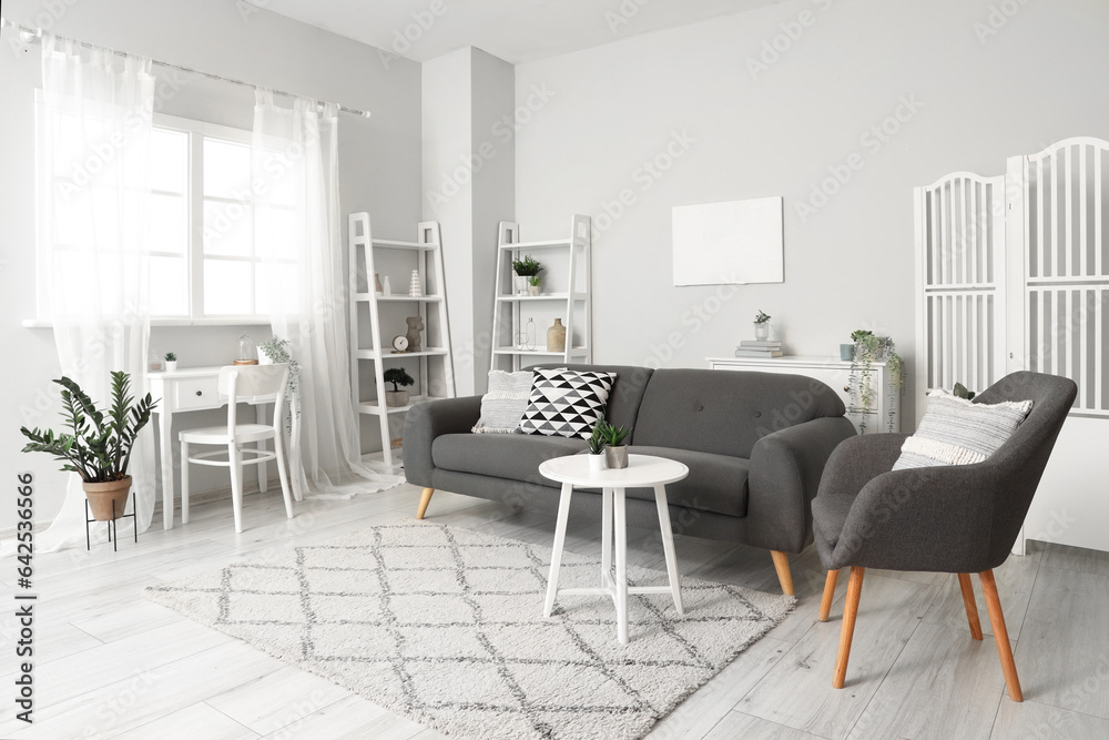 Interior of light living room with cozy armchair and grey sofa