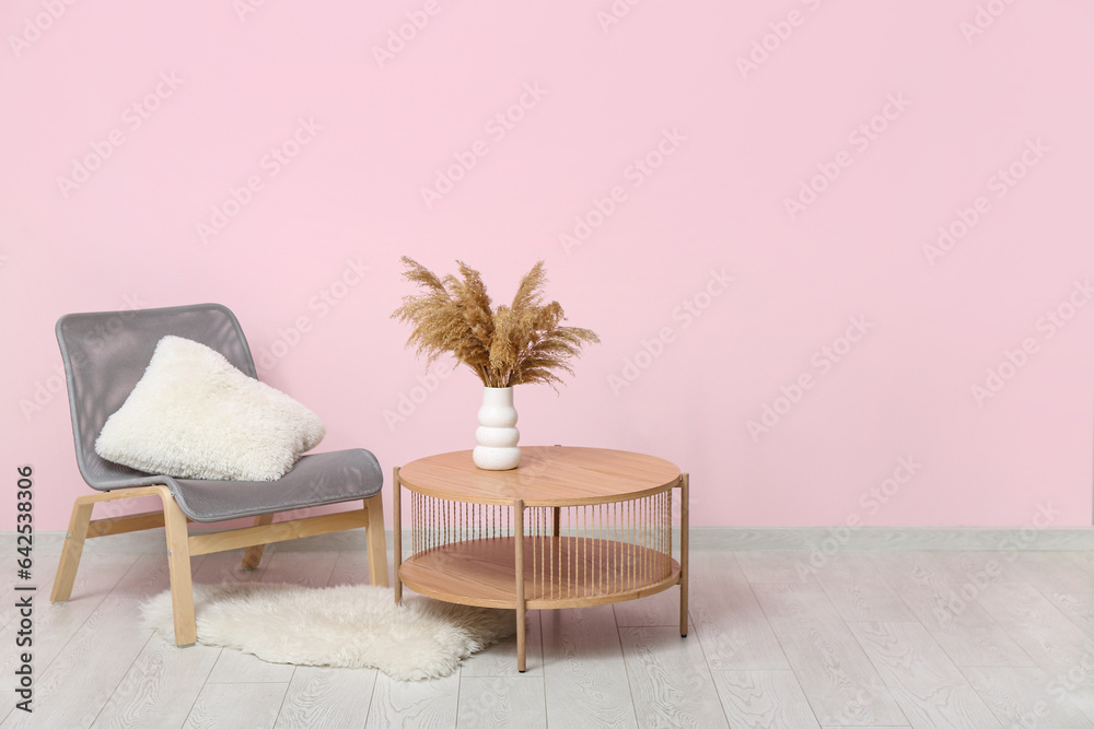 Comfortable armchair and wooden table with pampas grass near pink wall