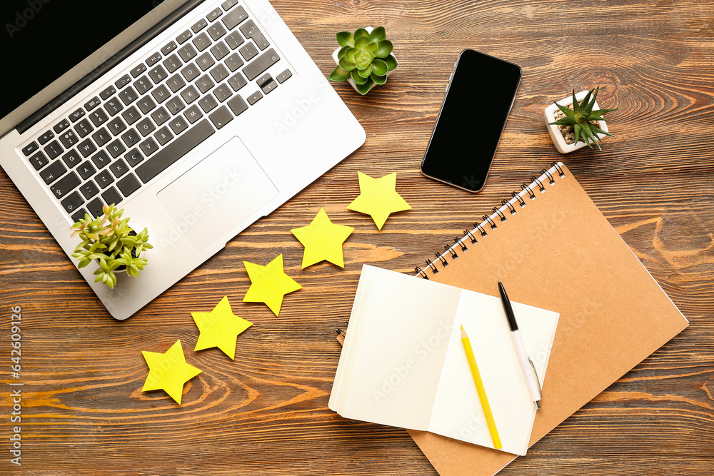 Five stars with laptop, notebooks and mobile phone on wooden background. Customer experience concept