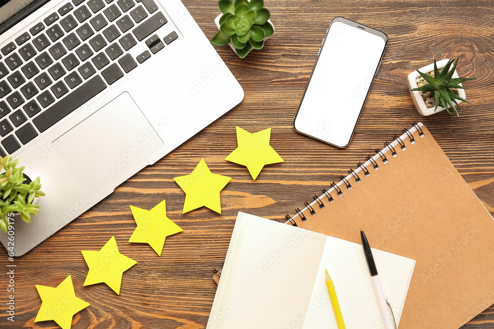 Five stars with laptop, notebooks and mobile phone on wooden background. Customer experience concept