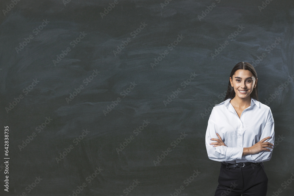 Attractive young european businesswoman with folded arms standing on empty chalkboard background wit