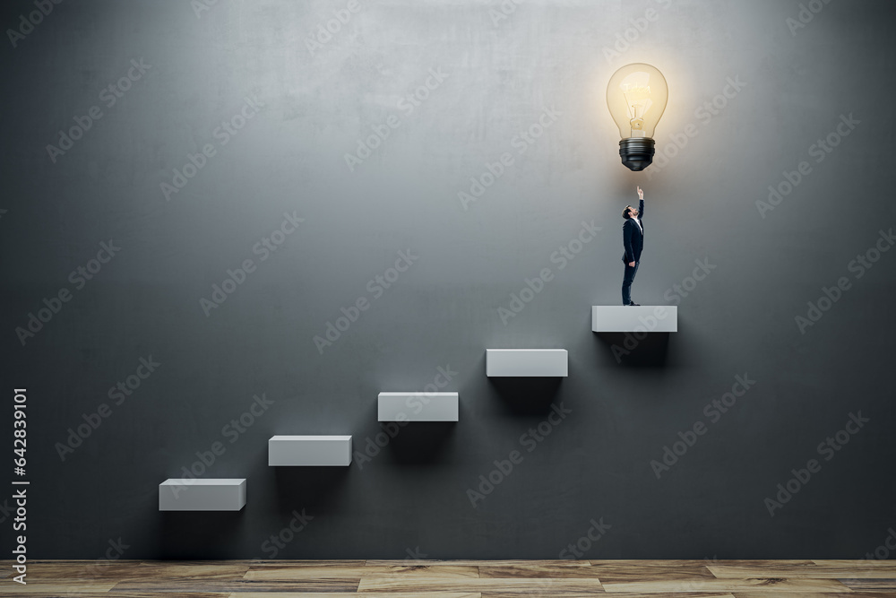 Side view of young man pointing at illuminated light bulb stairs to success on concrete wall backgro