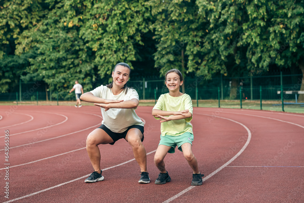 Mother and little daughter are doing exercise in the stadium.