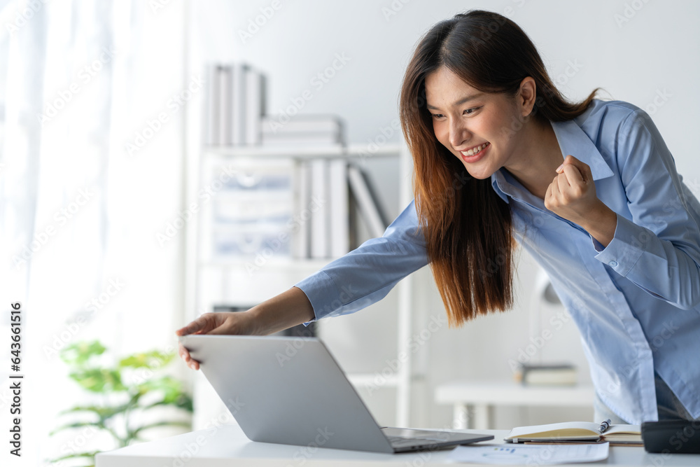 Happy Asian businesswoman standing at her desk in office Received information from laptop computer o