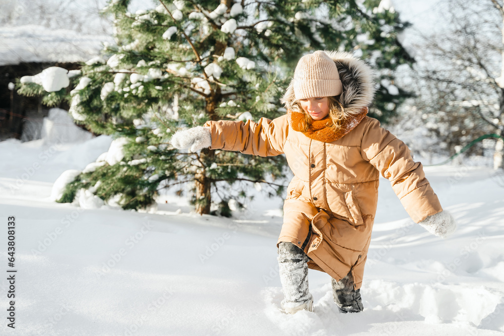 Little cute girl in white hat,scarf snood is lying,playing in snow. Kid walking in beautiful frozen 