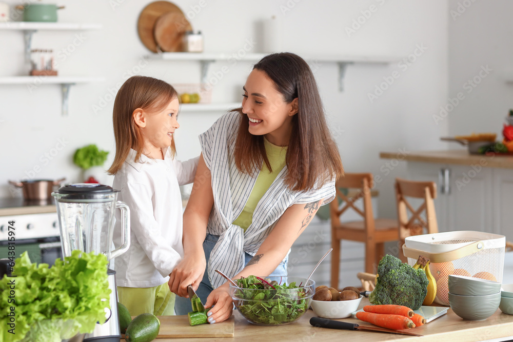 Little girl with her mother cutting cucumber in kitchen