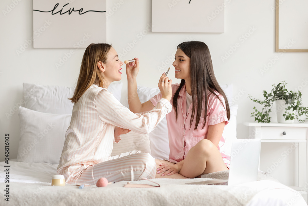 Female friends doing makeup in bedroom